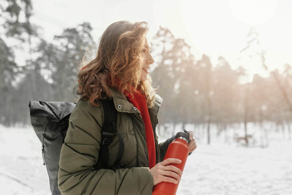 woman walking in snowy city at night holding thermos looking refreshed and glowing